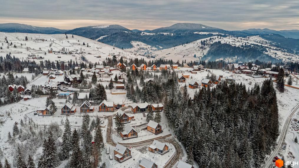 Зимовий вид на Котеджне містечко SKOGUR з дерев'яними котеджами. Засніжені гори та ліс навколо.