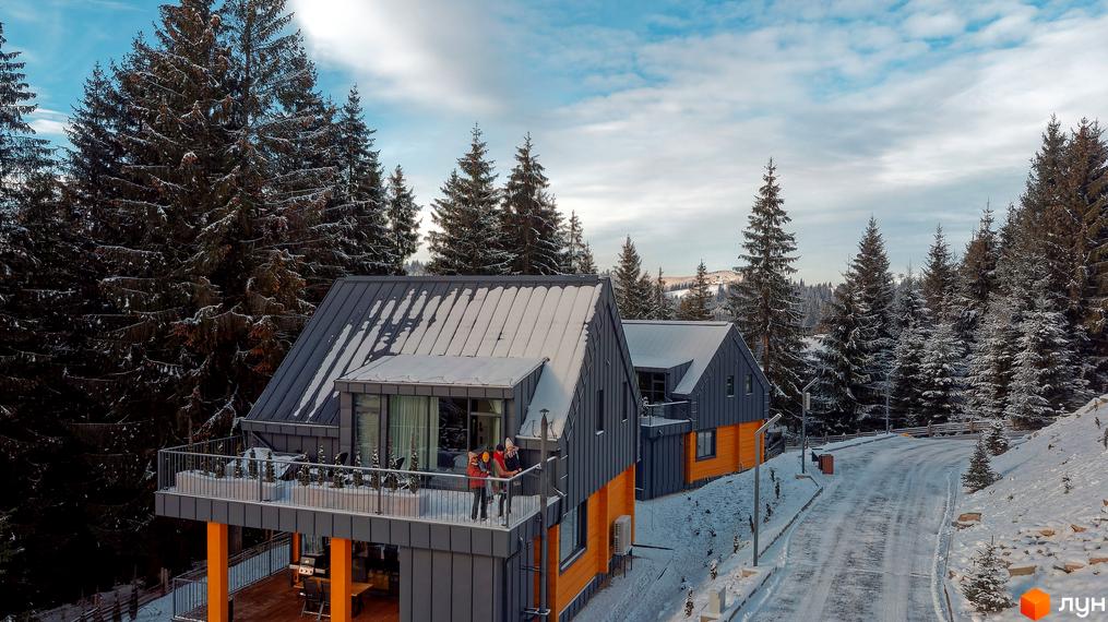 Зображення Котеджного містечка SKOGUR з видом на будинок з терасою та засніжені дерева. Зимовий пейзаж та дорога поруч.