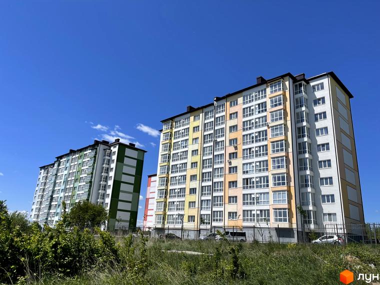Житловий комплекс Левада Дем’янів лаз. Багатоповерхові будинки з яскравим фасадом на тлі блакитного неба. Навколо зелені насадження та паркан.