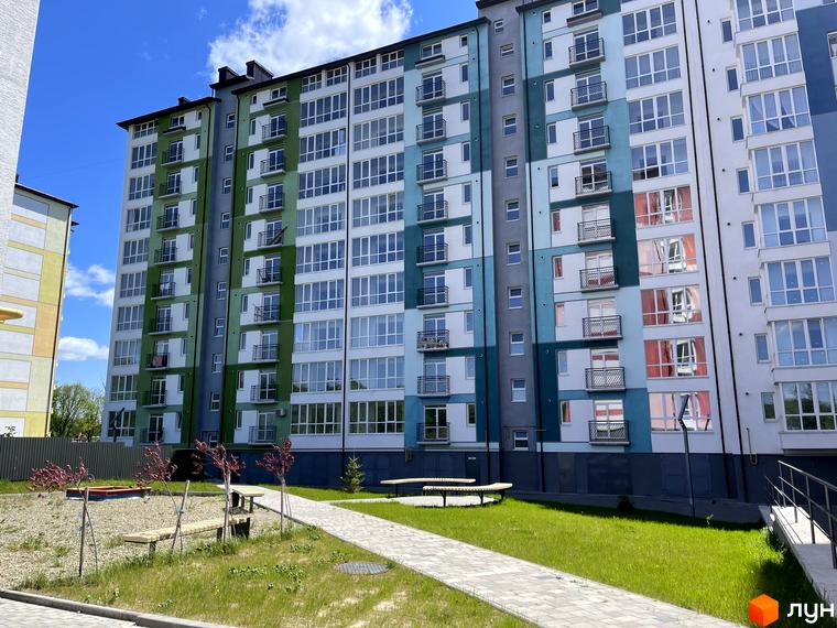 Новобудова ЖК Левада Дем’янів лаз з різнокольоровими фасадами та балконами. Поруч розташований доглянутий двір з лавками та пішохідною доріжкою.