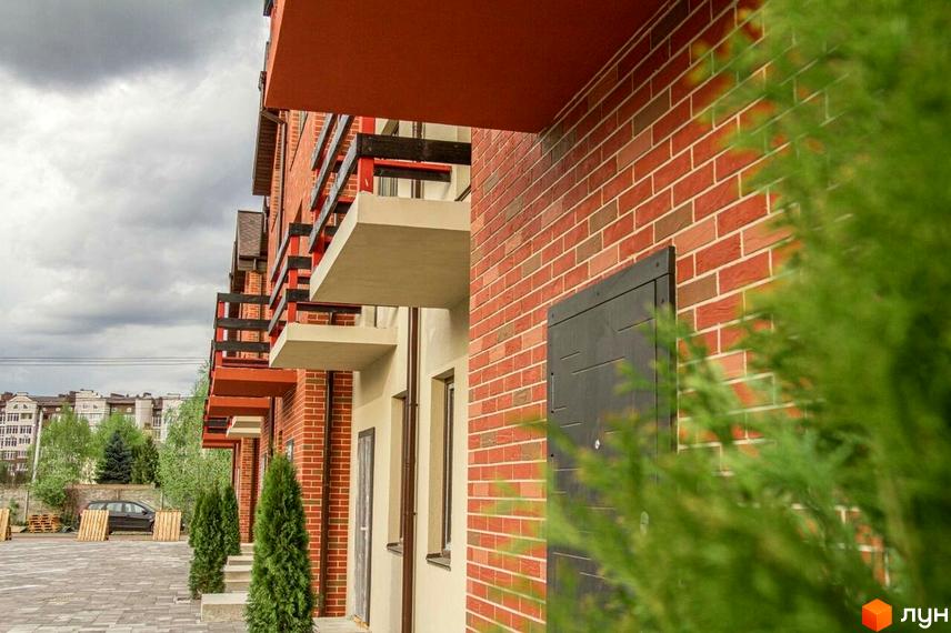 Цегляний фасад таунхаусів Modern House. На передньому плані зелені дерева та бруківка, на задньому - інші будівлі.