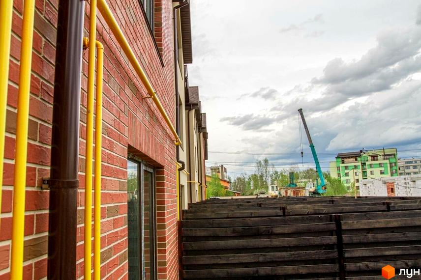 Цегляний будинок Modern House з жовтими трубами на фасаді. Поруч дерев'яний паркан та будівельний кран на тлі.