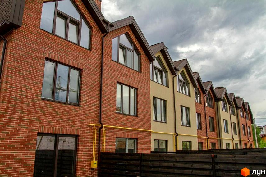 Цегляні будинки з великими вікнами в житловому комплексі Modern House. На передньому плані дерев'яний паркан, а на задньому - похмуре небо.