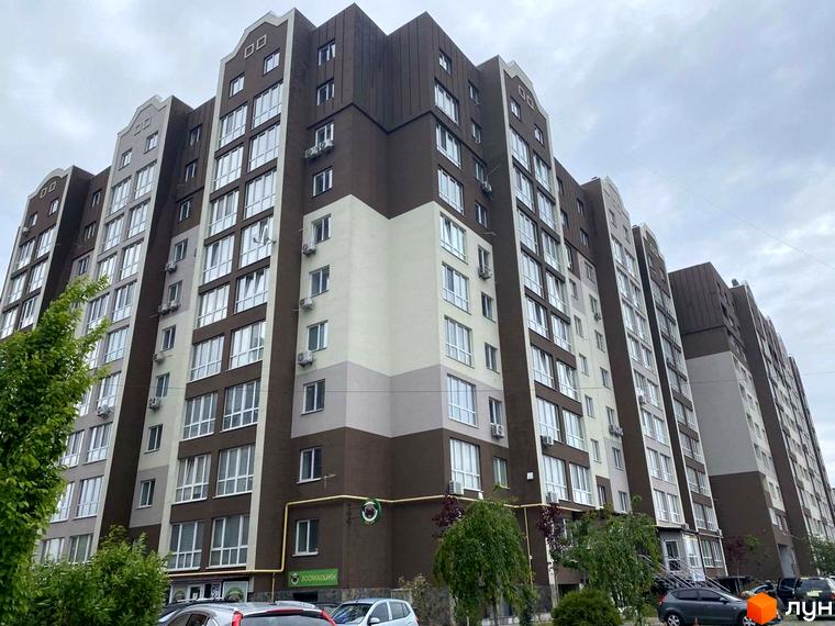 Новобудова ЖК Нова Конча-Заспа з коричнево-білим фасадом та численними вікнами. Перед будинком розташовані дерева та припарковані автомобілі.
