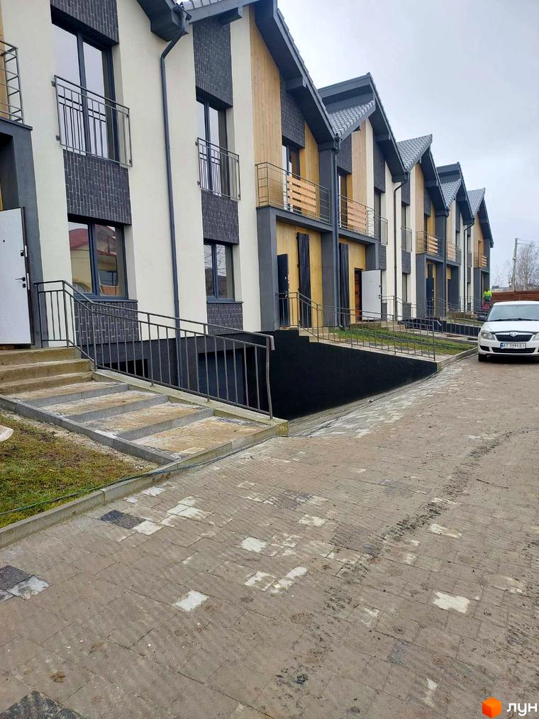 Зовнішній вигляд таунхаусів Noble House з бетонними сходами та бруківкою перед будинком. Комплекс має сірі дахи та дерев'яні елементи.