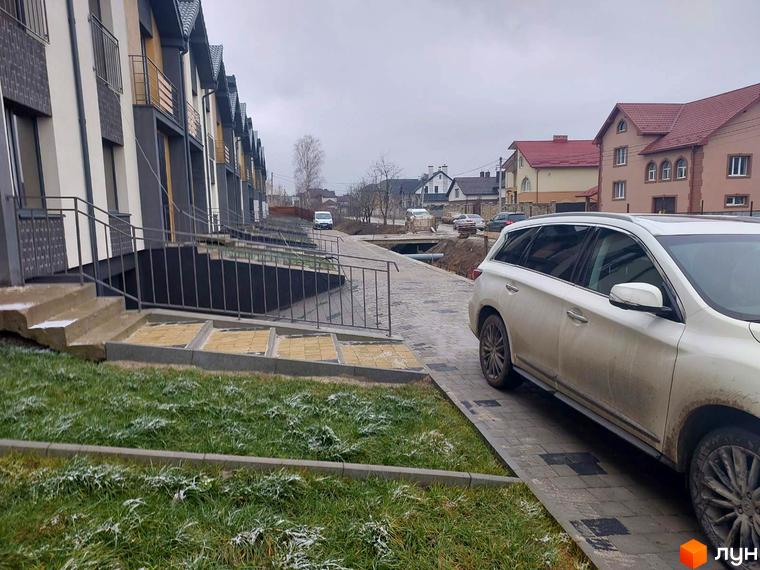 Ряд Таунхаусів Noble House з балконами та темними дахами. Перед будинками видно бруківку, припаркований автомобіль та зелену траву з інеєм.