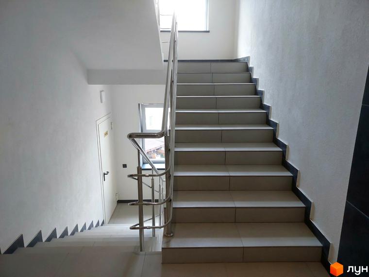 Сходи в клубному будинку Kovcheg Residence з металевими поручнями. Білі стіни та світлі сходи створюють відчуття простору.