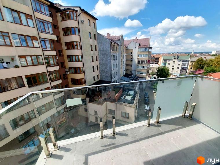 Вид з балкона на клубний будинок Kovcheg Residence з скляною огорожею та сусідні будівлі. Навколо багатоповерхові будинки та міський пейзаж.