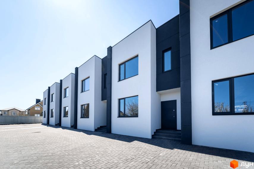 Зовнішній вигляд новобудови на вул. Полтавська, 15: білі фасади з темними акцентами, панорамні вікна та бруківка на прибудинковій території.