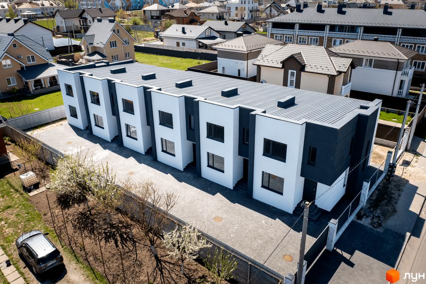 Сучасний житловий комплекс на вул. Полтавській, 15, з біло-сірими фасадами та пласкими дахами. На прибудинковій території розташовані бруківка, дерева та автомобіль.