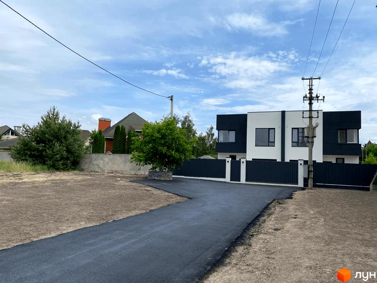 Новобудова на пров. Каштановий з чорно-білим фасадом та сірим парканом. Поруч асфальтована дорога та зелені насадження.