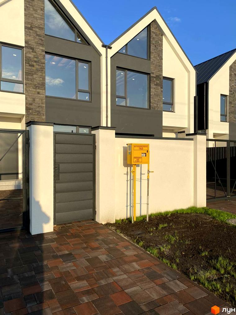 Зовнішній вигляд новобудови на вул. Княгині Ольги, 61, з сірим фасадом, кам'яними вставками та прибудинковою територією з бруківки та зеленими насадженнями.