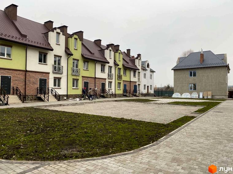 Таунхауси „Нова Конча-Заспа“: ряд будинків з світло-зеленими та білими фасадами, коричневими дахами. Прибудинкова територія з бруківкою та газоном.