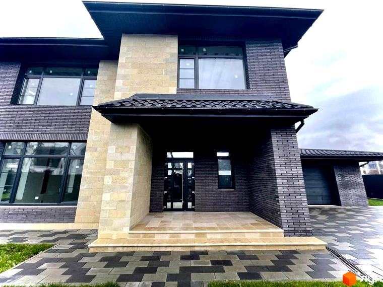 Котеджне містечко КМ Spacious HOME. Фасад будинку оздоблений темною цеглою та світлим каменем, перед будинком вимощена доріжка з плитки.