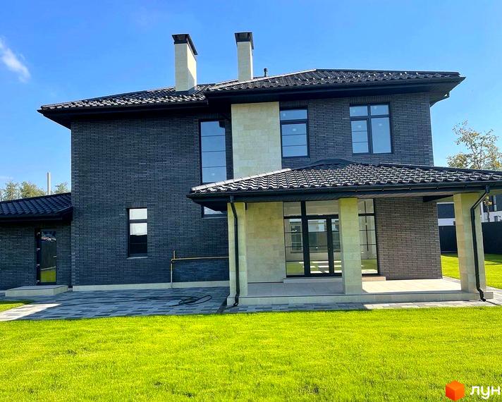 Котеджне містечко КМ Spacious HOME. Двоповерховий будинок з темно-сірої цегли з білими димарями та великими вікнами, розташований на зеленій галявині.
