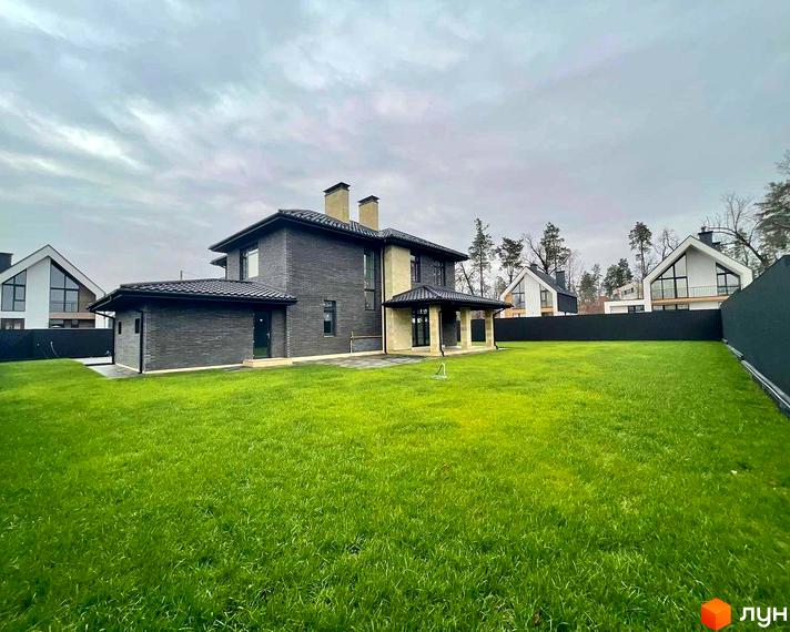 Котеджне містечко Spacious HOME: двоповерховий будинок з темної цегли та зелений газон. Навколо розташовані інші будинки та дерева.