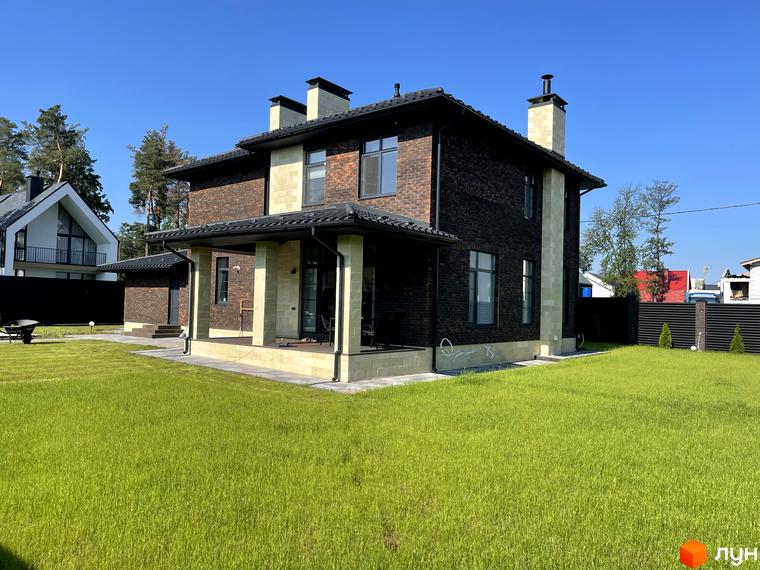 Котеджне містечко Spacious HOME. Двоповерховий будинок з цегляним фасадом темного кольору та світлими колонами на терасі, зелений доглянутий газон навколо.