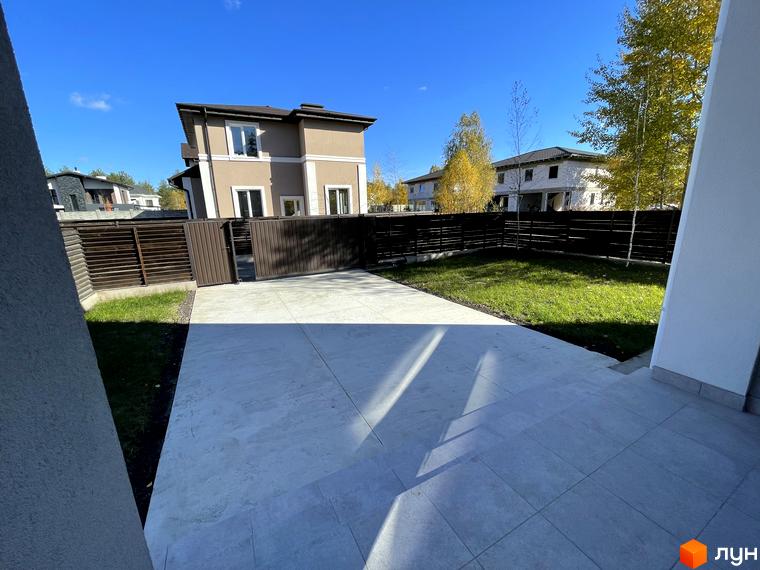 Котеджне містечко ForestK: двоповерховий будинок з коричневим фасадом та білими елементами, огороджена територія з газоном та вимощеним майданчиком.