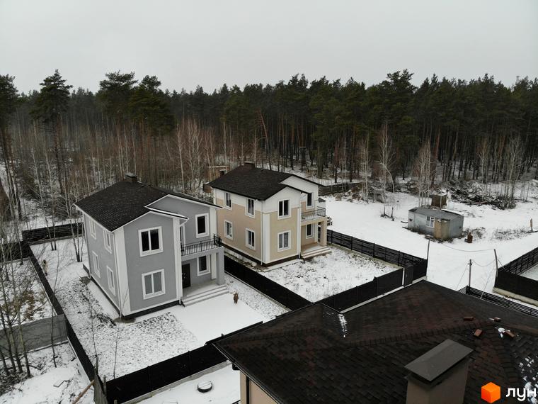 Котеджне містечко ForestK: двоповерхові будинки сірого та бежевого кольорів з темними дахами на тлі зимового лісу. Прибудинкова територія вкрита снігом, огороджена парканом.