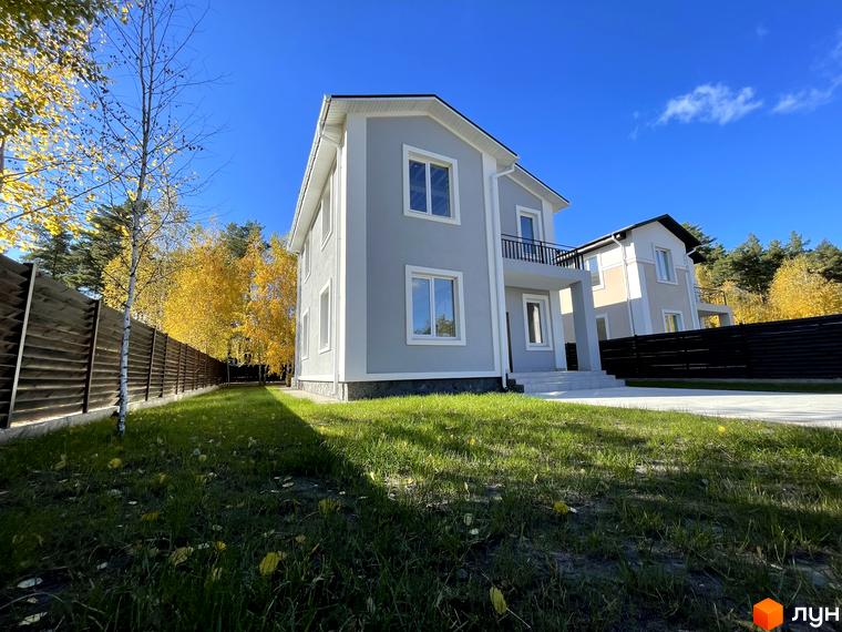 Котеджне містечко ForestK: двоповерховий будинок світло-сірого кольору з білими вікнами та балконом, на тлі осінніх дерев та блакитного неба.