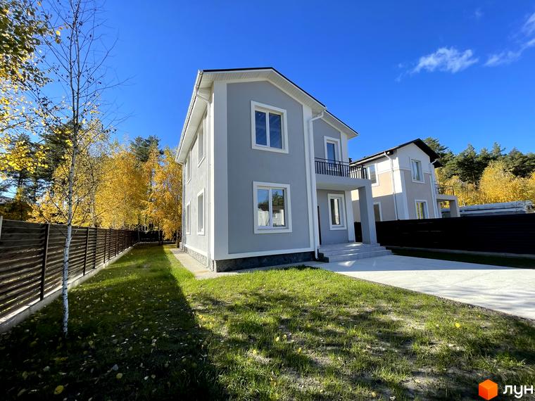 Котеджне містечко ForestK: двоповерховий будинок сірого кольору з білими вікнами та балконом на другому поверсі. Навколо будинку зелена галявина та дерев'яний паркан.