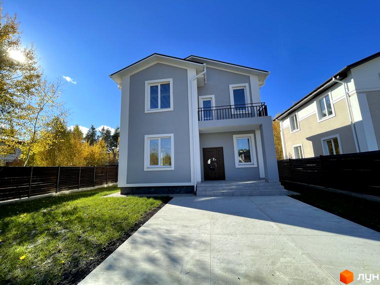 Котеджне містечко ForestK: сірий двоповерховий будинок з білими вікнами та балконом, доглянутий газон та бетонна доріжка перед будинком.