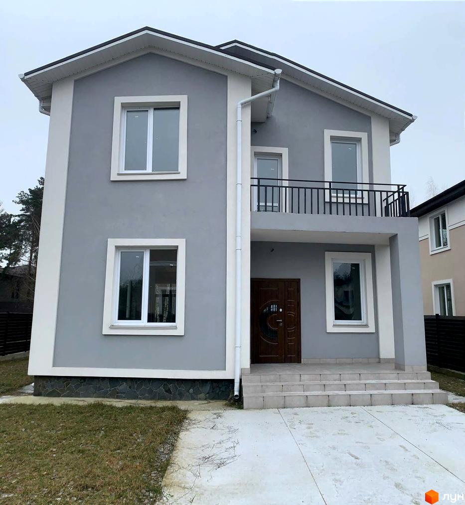 Зовнішній вигляд будинку в Котеджному містечку ForestK з сірим фасадом та білими елементами. Навколо будинку облаштована прибудинкова територія з газоном та бетонною доріжкою.