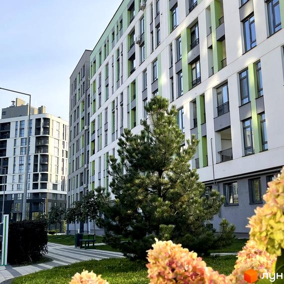 Новобудова ЖК Пасічний з біло-зеленими фасадами та балконами. На прибудинковій території зелений газон, дерева та квіткові клумби.