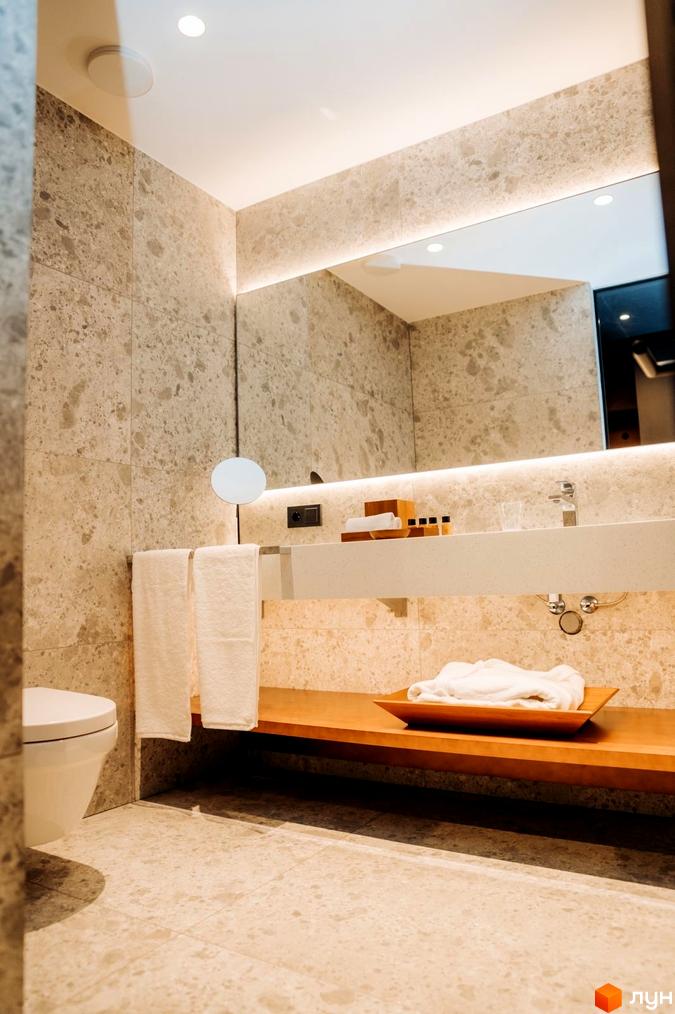 Інтер'єр ванної кімнати в апарт-комплексі LEV RESORT HOTEL. Світлі стіни, велике дзеркало, дерев'яні елементи та біла сантехніка.