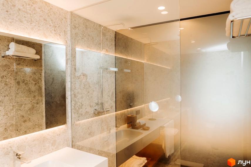 Інтер'єр ванної кімнати в апарт-готелі LEV RESORT HOTEL. Світла плитка, дзеркало, душова кабіна зі скляними стінами, раковина.