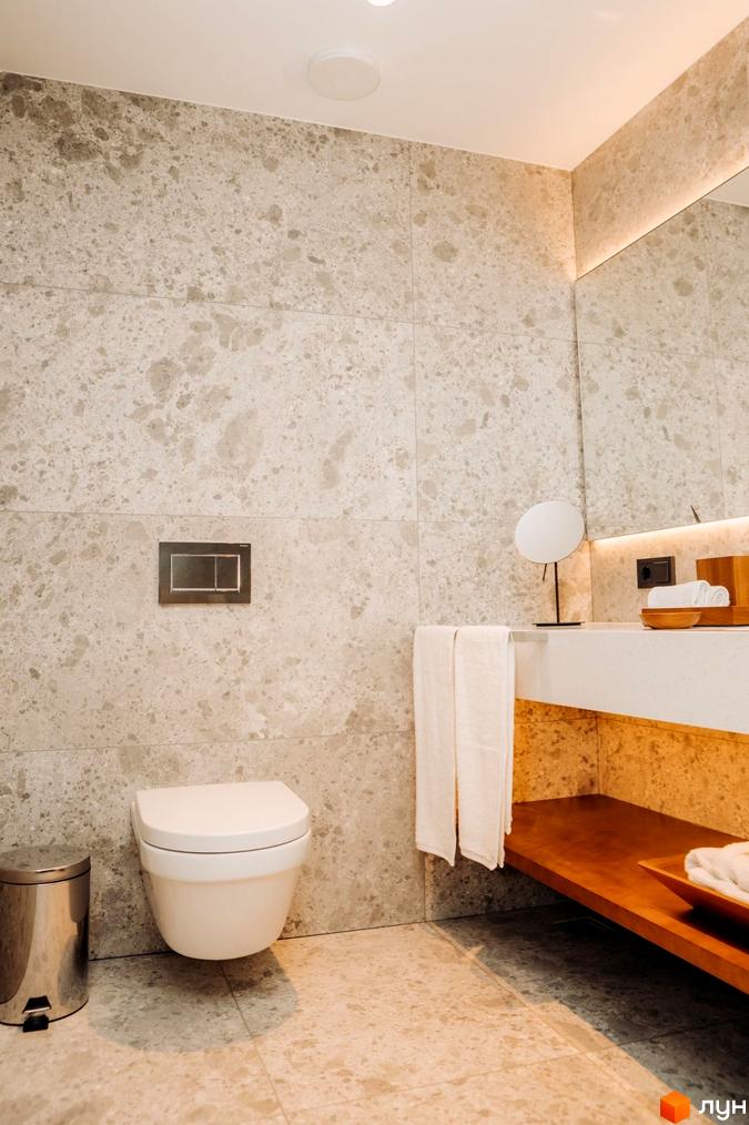 Інтер'єр ванної кімнати в апартаментах LEV RESORT HOTEL. Світлі стіни з великою плиткою, підвісний унітаз, тумба з дерев'яною полицею.
