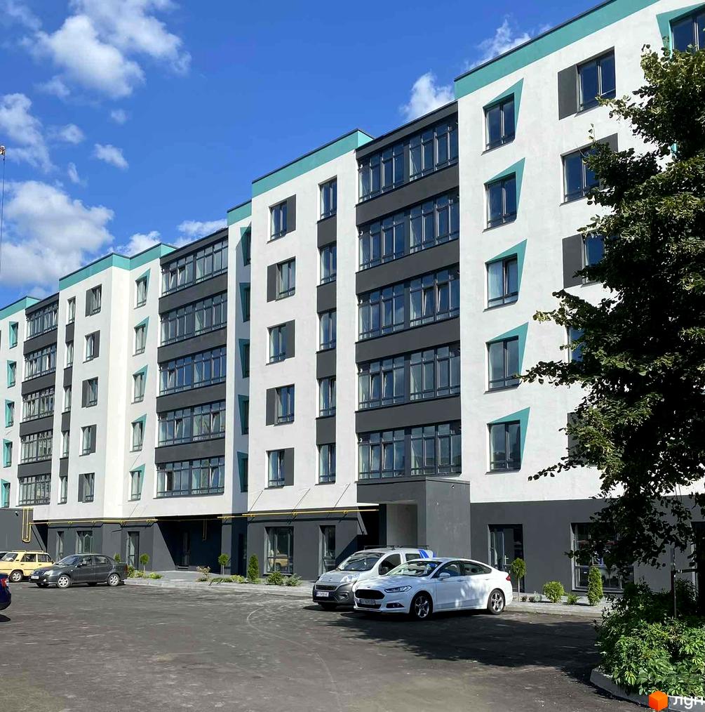 Зовнішній вигляд новобудови ЖК SkyCity з біло-сірими фасадами та бірюзовими акцентами. Перед будинком розташований паркінг з автомобілями.