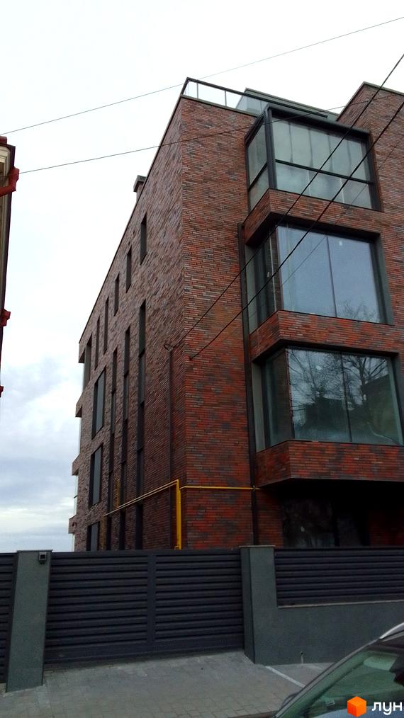 Будинок з червоної цегли з великими вікнами та скляним дахом. Поруч розташована сіра огорожа.