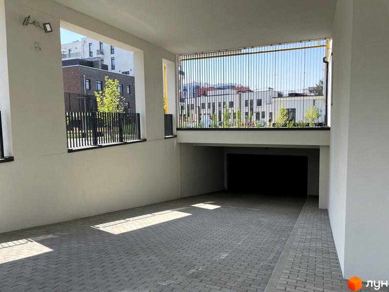 Зовнішній вигляд ЖК Villa Magnolia Spring: сучасний паркінг під відкритим небом з бруківкою та огорожею. Територія комплексу з зеленими насадженнями та будівлями на фоні.