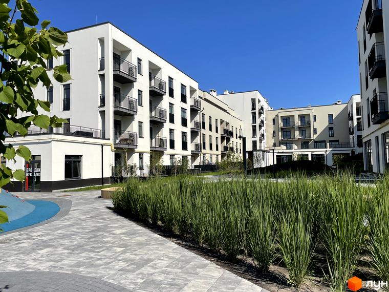Житловий комплекс Villa Magnolia Spring з білими фасадами, балконами та зеленою прибудинковою територією. Сучасна архітектура новобудови та доглянутий двір.