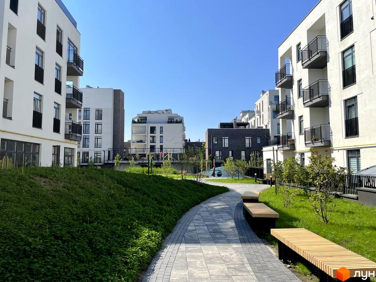 Житловий комплекс Villa Magnolia Spring з білими фасадами, балконами та зеленим ландшафтом. На території є доріжки та дерев'яні лавки для відпочинку.