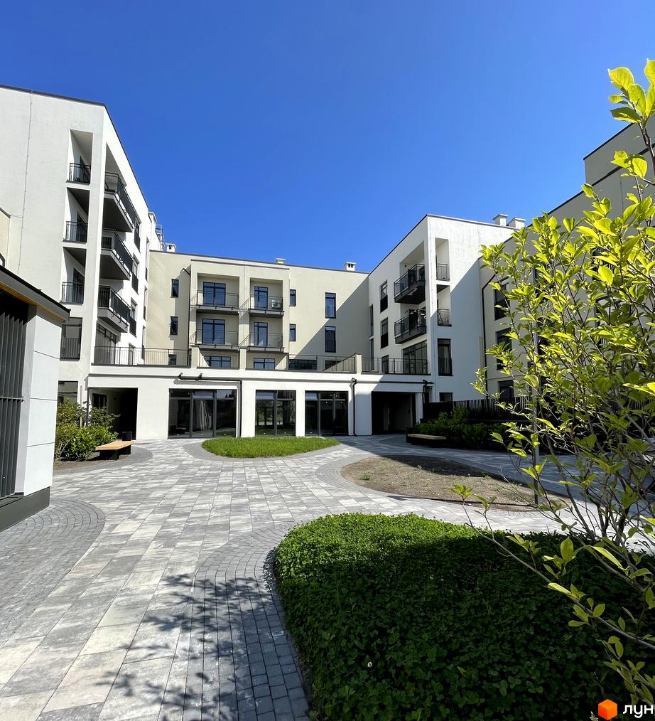 Житловий комплекс Villa Magnolia Spring: білі фасади будівель з балконами та панорамними вікнами. Прибудинкова територія з бруківкою, зеленими насадженнями та місцями для відпочинку.