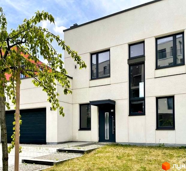 Житловий комплекс Villa Magnolia. Фасад будинку з великими вікнами та темними рамами, вхідні двері з навісом. Поруч розташовані гаражні ворота та зелена зона з деревом.