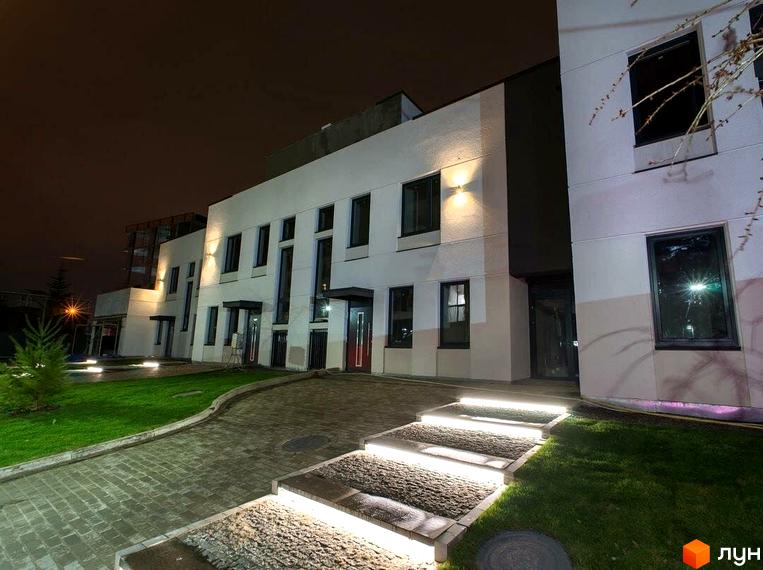 Зовнішній вигляд новобудови ЖК Villa Magnolia з підсвіченими сходами та доглянутою прибудинковою територією вночі. Опис фасаду будівлі та зеленої зони.