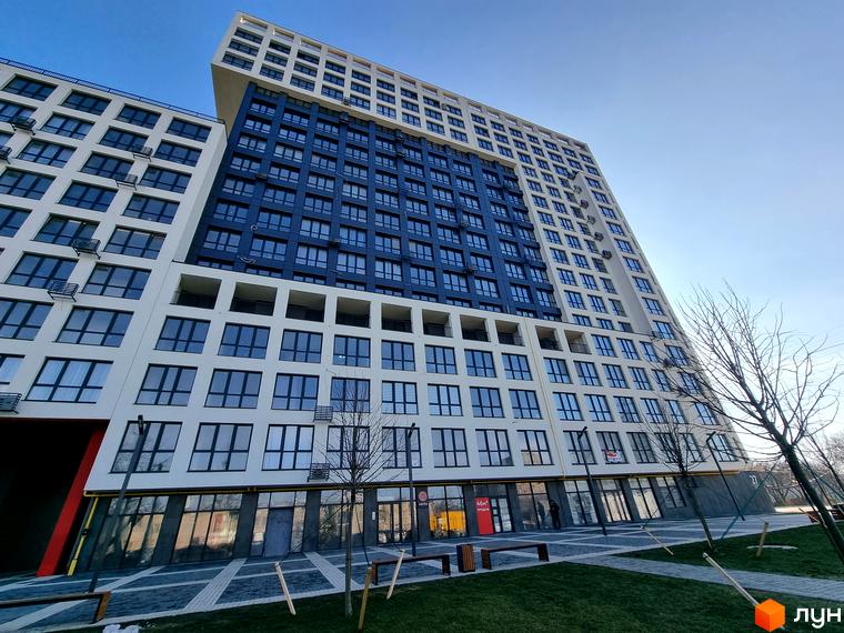 Зображення фасаду та прибудинкової території Житлового комплексу Вільне Місто. Висотна будівля з великою кількістю вікон та озелененим подвір'ям.