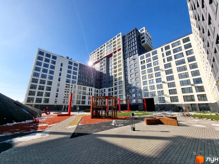 Зображення фасаду та подвір'я Житлового комплексу Вільне Місто. На фото багатоповерховий будинок з великою дитячою площадкою.