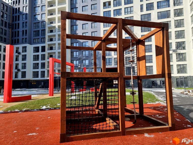 Багатоповерхові будинки Житлового комплексу Вільне Місто з світлими та темними фасадами. На прибудинковій території дитячий майданчик з дерев'яним ігровим комплексом.