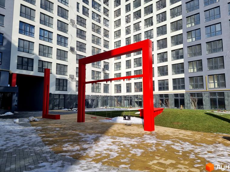 Зовнішній вигляд ЖК Вільне Місто з великими вікнами. На передньому плані дитячий майданчик з гойдалками та зелена зона для відпочинку.