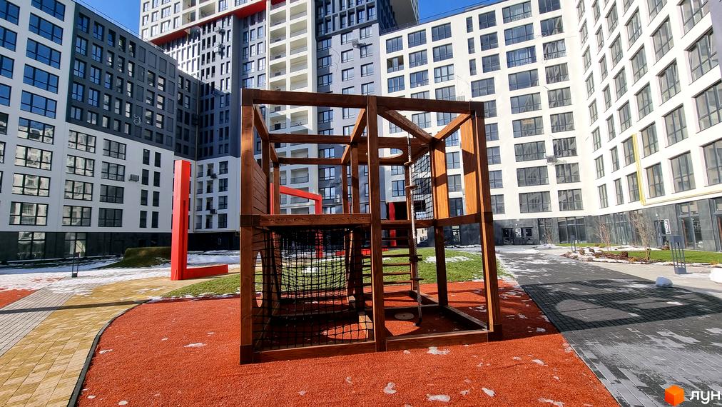 Багатоповерхові будинки Житлового комплексу Вільне Місто з біло-сірими фасадами. На прибудинковій території є дерев'яний дитячий майданчик та вимощені доріжки.