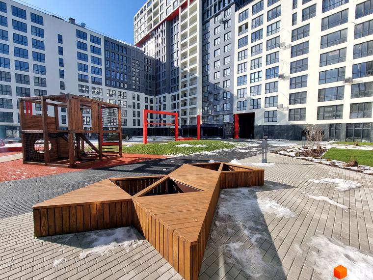 Зображення фасаду та двору Житлового комплексу Вільне Місто. Вигляд новобудови з дитячим майданчиком та лавками.