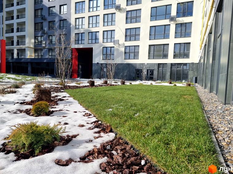 Новобудова Вільне Місто: багатоповерхові будинки з білими та сірими фасадами, червоними акцентами. Прибудинкова територія з зеленим газоном та снігом.