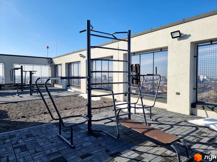 Світлі фасади Житлового комплексу Вільне Місто з вікнами та металевими решітками. На даху облаштовано відкритий спортивний майданчик з тренажерами.