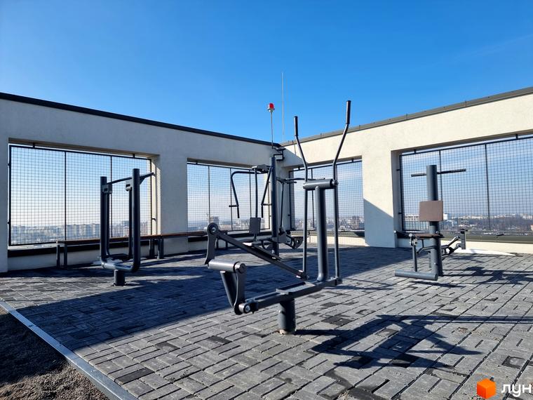 Тераса Житлового комплексу Вільне Місто з білими стінами та металевими огорожами, де розташовано відкритий спортмайданчик з видом на місто.