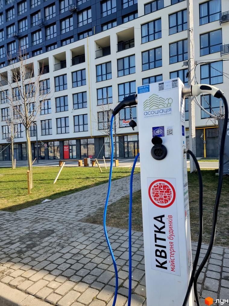 Сучасна новобудова ЖК Вільне Місто з зарядними станціями для електромобілів на прибудинковій території. Зовнішній вигляд будинку з великою кількістю вікон та балконів.