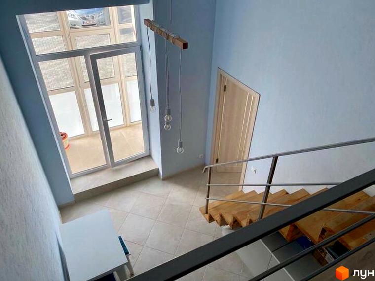 Інтер'єр в ЖК Сузір'я 2020: сходи з дерев'яними східцями, двері, вікна, підвісні лампи. Світлі стіни та плитка на підлозі створюють відчуття простору.